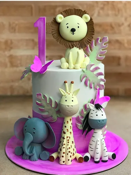 A sweet and colorful jungle animal cake for a first birthday. The combination of pink and purple with the cute fondant elephant, lion, and giraffe makes it a unique and lovely choice.