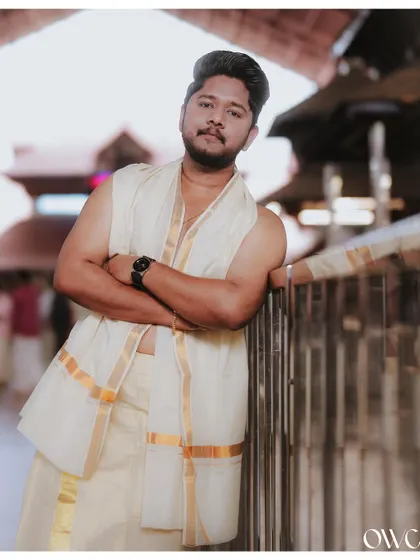 A stylish portrait of the groom in his traditional mundu, leaning against a railing at the temple.