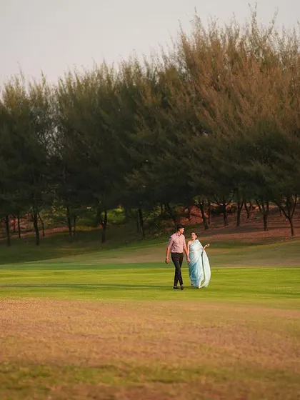 A beautiful wide shot of a couple walking across a vast green field at sunset, creating a serene and cinematic feel.