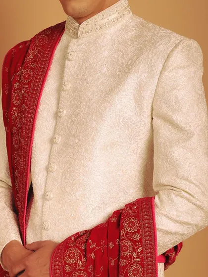 The beauty of a groom's attire is in the details. Here, you can see the intricate texture of the ivory sherwani fabric and the luxurious zardozi work on the border of the red velvet stole.