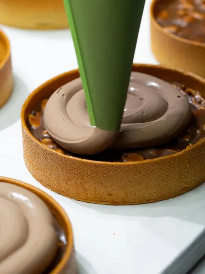 Piping a smooth, rich chocolate crémeux into a tart shell. Our hands-on classes ensure you master techniques like this for a perfect fill every time.