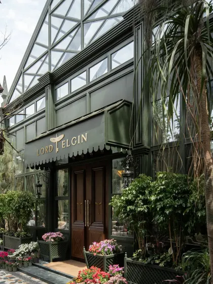 The entrance to the Lord Elgin Glasshouse, framed by lush planters. The deep green facade and classic wooden doors create a sense of arrival into a hidden, verdant world.