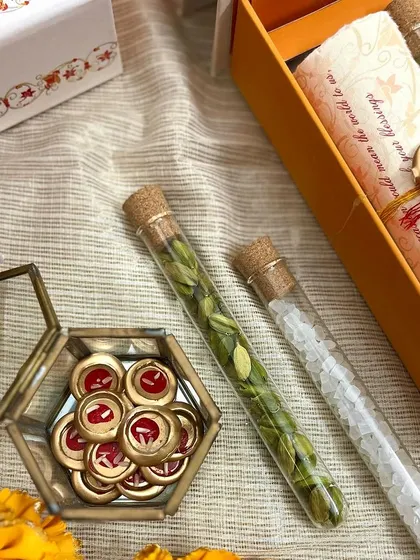 A close-up of the intricate details within the wedding invitation box, including the wax seals and the delicate glass tubes filled with cardamom and sugar crystals.