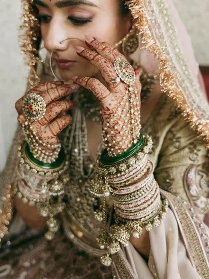 A close-up on the hands of the bride, showcasing the detailed henna, the stunning hathphool, and the mix of traditional green and pastel bangles that completed her look.