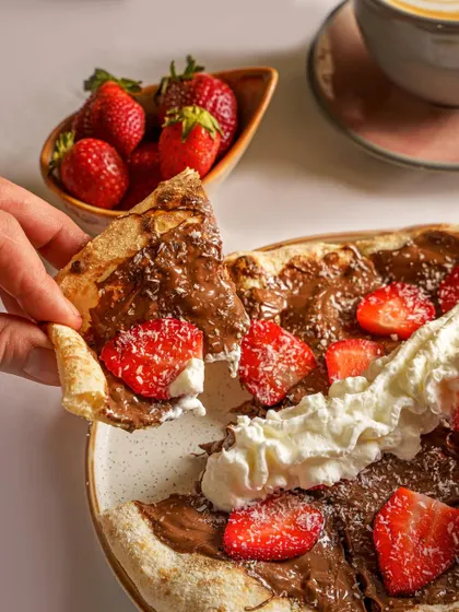 A decadent Nutella and strawberry dessert pizza. The close-up on the slice being pulled away creates a sense of indulgence and is perfect for a dessert menu feature.