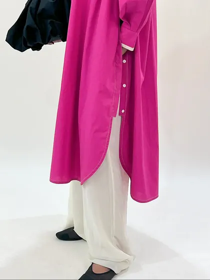 A detailed shot of the fuchsia longline shirt, showing its curved hem and button details.
