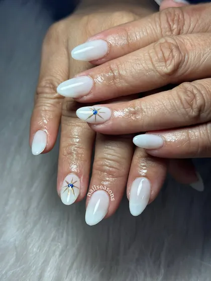 An elegant milky white manicure with a delicate, hand-painted evil eye starburst for a touch of protection and style.