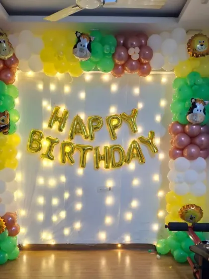 A simple jungle-themed decoration with animal foil balloons, a "Happy Birthday" banner, and a wall of fairy lights.