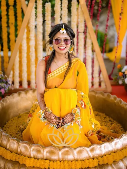 The bride during her haldi ceremony, her hands joined together, showcasing the beautiful henna stain.