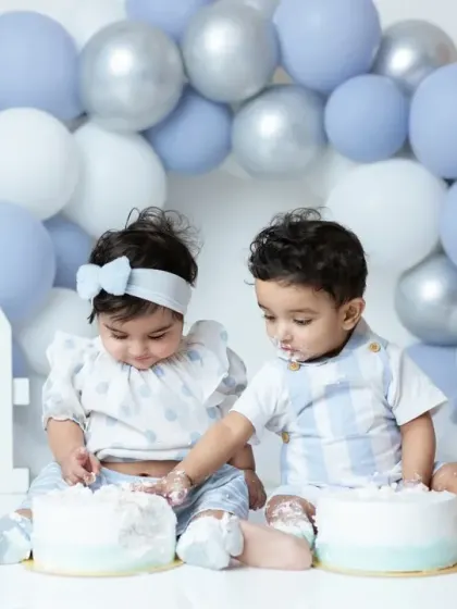 A fun and messy moment from a twin cake smash session. The siblings explore their first birthday cakes together in a coordinated blue and white setup.