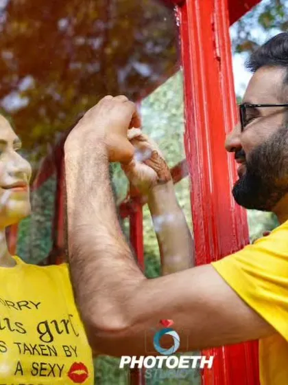 A creative shot using a reflection in a red phone booth window. The bride's quirky t-shirt adds a fun, personal touch to this pre-wedding photo.