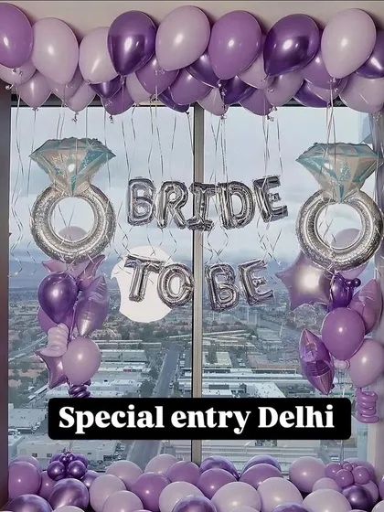 A fun and feminine 'Bride to Be' room decoration. This setup uses shades of purple balloons, large diamond ring foil balloons, and a city view from the window as a backdrop.
