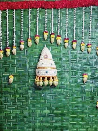A complete Varamahalakshmi pooja backdrop featuring a woven leaf mat and traditional flower hangings. The central floral piece, known as a 'kunjam', adds an authentic touch to the sacred setup.