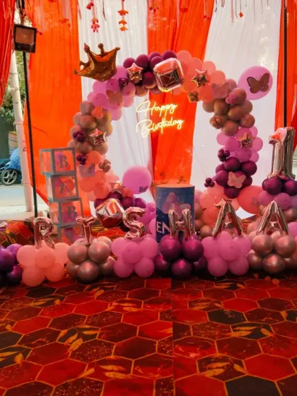 A first birthday setup with a circular balloon arch, a neon sign, and the name spelled out in individual balloon letters.