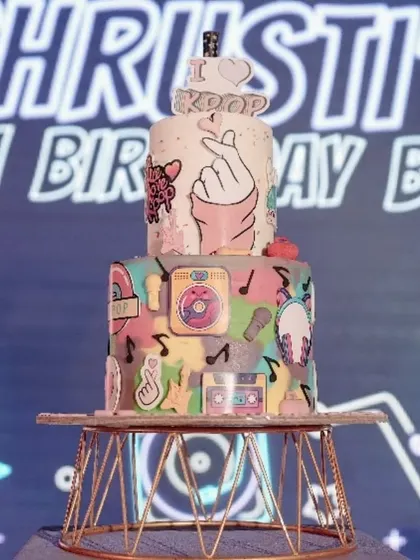 A fantastic K-Pop themed birthday cake. The two-tiered cake is decorated with musical notes, headphones, and the "I love K-Pop" sign, making it a perfect centerpiece for the celebration.
