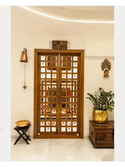 A full view of the traditional Pooja room doors, complemented by a brass temple bell and other ethnic decor pieces. This entrance sets a reverent tone for the space within.