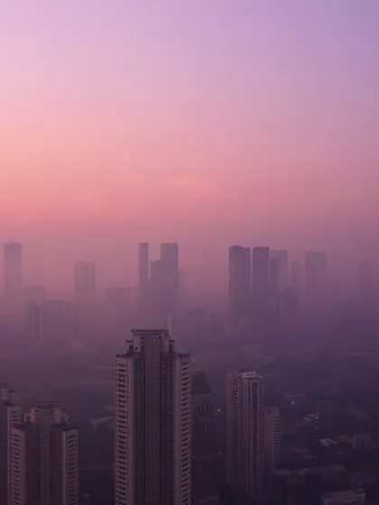 The upper portions of Mumbai's skyscrapers are silhouetted against a soft, hazy, purple and pink sky.