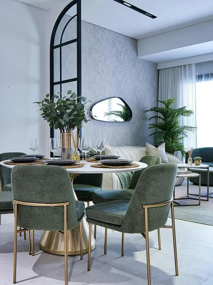 An elegant dining room featuring a round marble-top table and custom green velvet chairs with brass-finished legs. The design is both modern and luxurious.