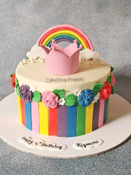 A splash of color with this rainbow-themed cake. It features fondant rainbow stripes around the base, topped with a fondant crown and rainbow, and surrounded by small sugar flowers.