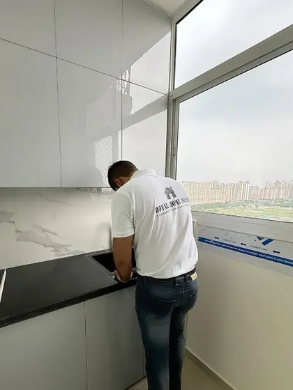 Here I am inspecting the sink area in a newly installed kitchen. The large window provides plenty of natural light, complementing the white and grey color scheme.