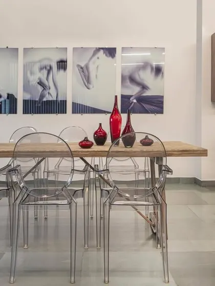 Another view of the fashion showroom's conference area, this time against a clean white wall. The transparent chairs and rustic table are complemented by minimalist art, showcasing the space's versatility and modern elegance.
