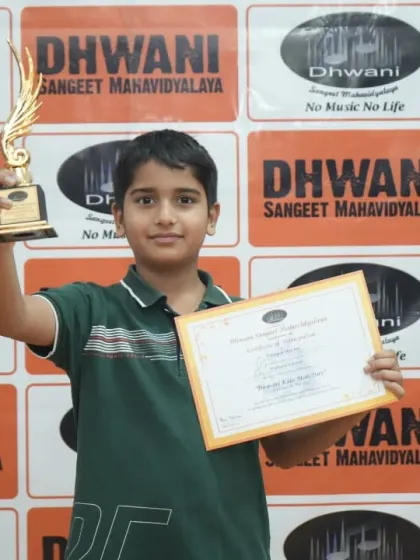 A young student proudly holds his certificate and trophy.