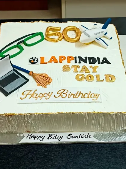 A 50th birthday cake for a colleague, personalized with inside jokes and favourite items like a laptop, glasses, and an airplane.