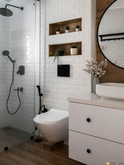 Another view of the bathroom, showing the walk-in shower with a glass partition and modern black fixtures. The built-in wall niches provide stylish storage for toiletries.