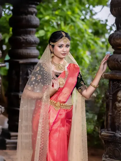 This image captures the regal elegance of a bride adorned in traditional temple jewellery against a historic backdrop. The gold pieces stand out beautifully against the red saree.