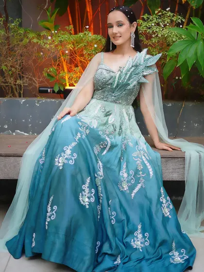 A breathtaking ombre gown in shades of sea green and blue, featuring silver embroidery and a unique one-shoulder leafy cape detail.