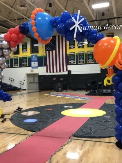 A creative space-themed balloon arch designed for a large venue like a school gym. The arch features balloon sculptures of planets and spaceships, creating an impressive focal point.