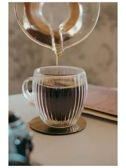 A pour-over coffee being decanted into a glass mug. This shot captures the process and craft of coffee making, appealing to cafe culture enthusiasts.