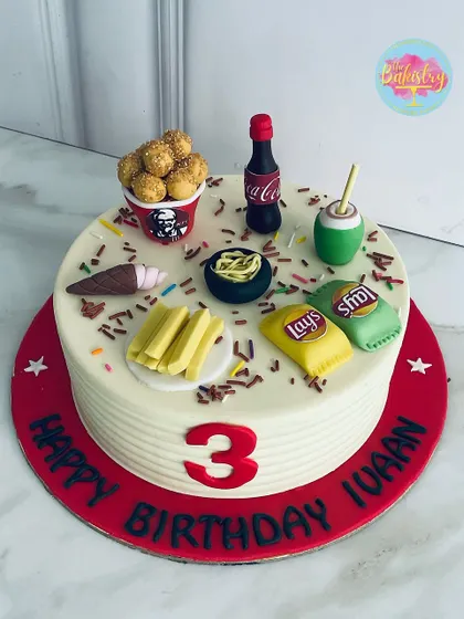 A feast for the eyes and taste buds! This fun fast-food-themed cake for a 3rd birthday is topped with all the favorites: KFC chicken, Lays chips, Coke, and fries, all in edible form.