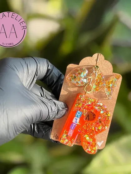 A close-up of a custom initial keychain with a name. The glitter and charm make it a fun and sparkly accessory.