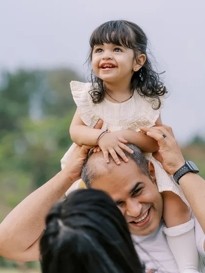 A daughter's joyful smile as she sits on her father's shoulders. These are the happy, carefree moments of childhood.