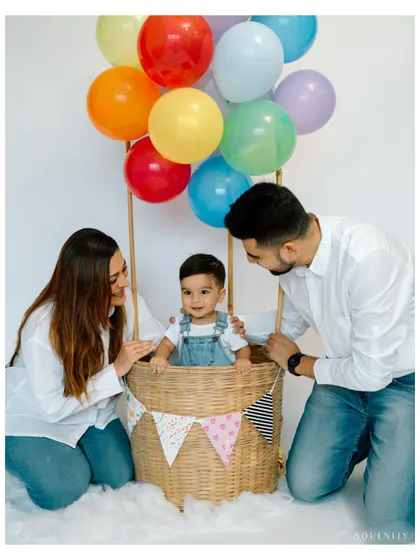 The whole family joins the adventure! Parents help their little one get ready for his hot air balloon ride in this heartwarming group shot.