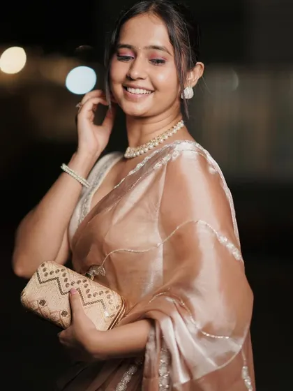Elegance and grace for an evening affair. This beautiful beige organza saree with delicate handwork is perfect for a classy, understated look. Pair it with pearls to complete the ensemble.