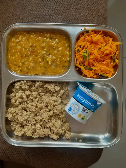 A beautiful vegetarian plate with quinoa, dal, and a vibrant carrot salad, complemented by a serving of Greek yogurt. This meal is light, nutritious, and full of flavor.