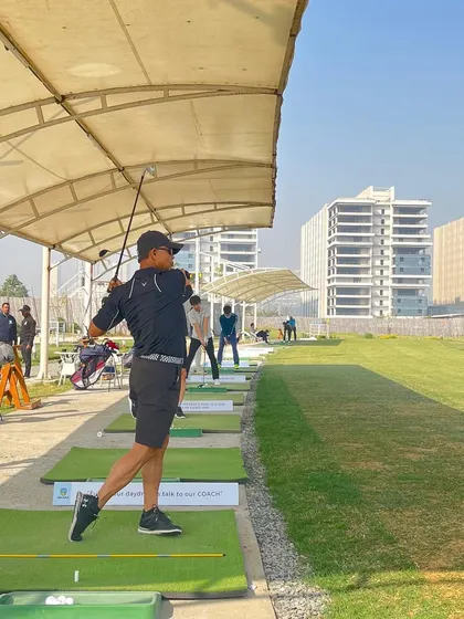 A player takes a full swing from one of our covered hitting bays, with the expansive range and city skyline in the background.