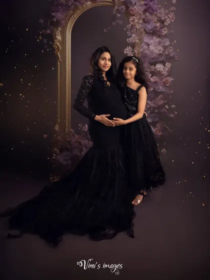 An elegant studio portrait of a mother and daughter. The coordinated black dresses and the soft, sparkling lights create a sophisticated and timeless image celebrating their bond before the new arrival.