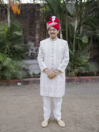 A full-length portrait of the groom, showcasing his complete wedding outfit from the turban to the shoes.