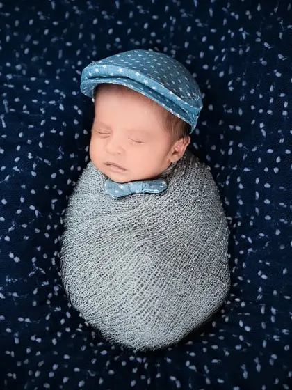 A dapper little newborn wearing a bow tie and a newsboy cap while swaddled. This shows how we can add a touch of personality and fun to newborn shoots.