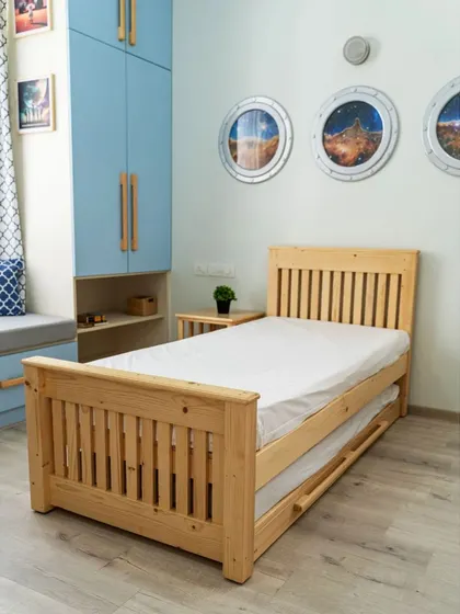 The trundle bed in its compact form, showcasing the beautiful natural pine wood and classic slatted design of the headboard and footboard.