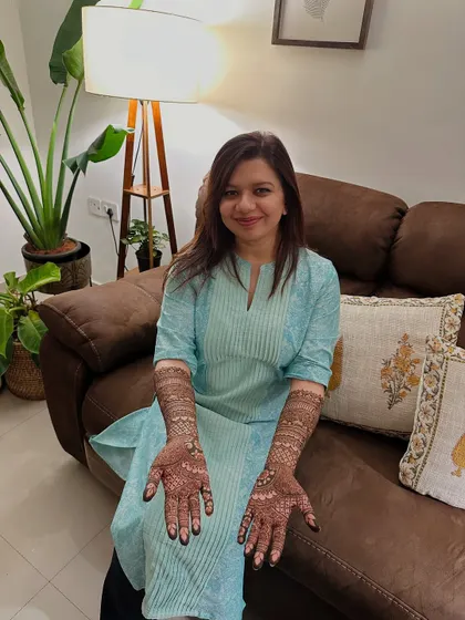 A smiling bride showing her completed full-arm mehndi designs.