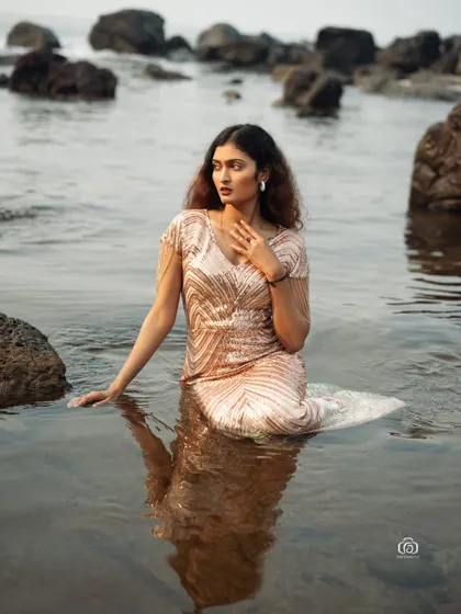 A thoughtful pose in a glamorous gown, with the model sitting in the water. The combination of the elegant dress and the natural ocean environment is both beautiful and unique.