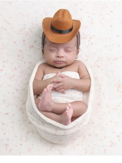 A little cowboy in a simple setup. The focus remains on the baby's adorable pose and tiny cowboy hat in this minimalist portrait.