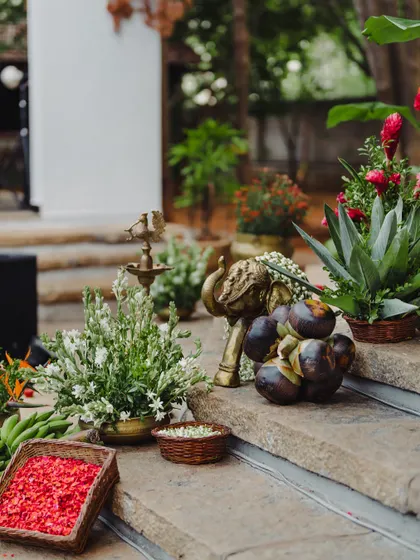 A collection of traditional decor items, including brass elephants, palm fruits, and floral arrangements, styled on stone steps.