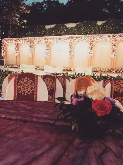 A classic wedding reception setup with an arched floral backdrop. The seating is arranged with custom printed chair covers, showing how we coordinate every detail to match the overall theme.