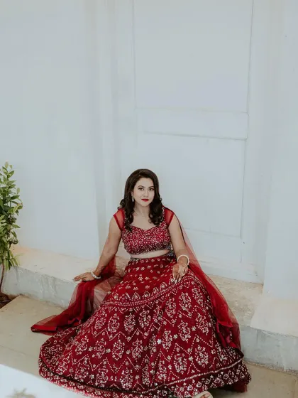 A modern engagement look featuring a deep red lehenga with intricate silver embroidery. The bride's hair is styled in soft, open waves for a contemporary and glamorous feel.
