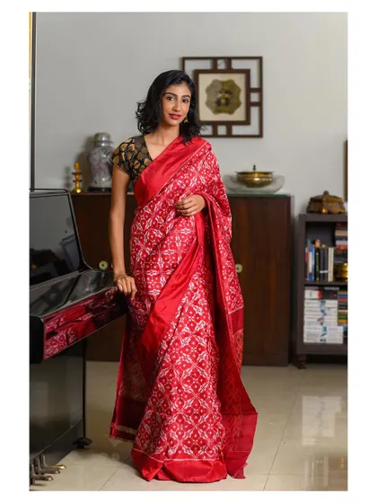 An elegant indoor portrait in a beautiful red saree. The model is seated next to a piano, adding a classical and sophisticated element to the scene.